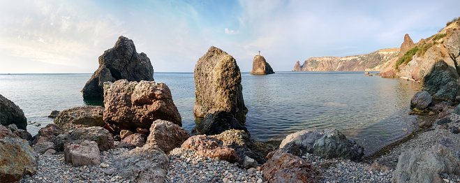 Sea shore with red coastal cliffs, rocks in water on a background of the sky in morning, panoramic view
