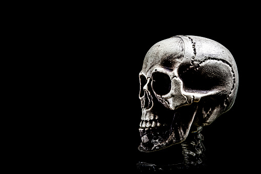 Human skeleton skull in dramatic low key light, corona covid-19 against pitch black background