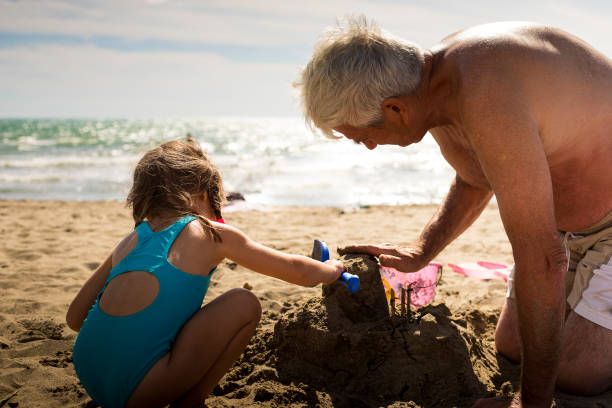 großvater und enkelin spielen mit sand am strand. - lifestyles child beach digging stock-fotos und bilder