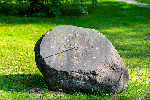 An old sundial made of a large stone with a metal rod, the clock will start at 4 PM.