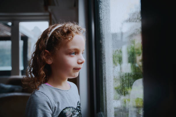 istock Bored girl standing near window looking at rain 1272378461