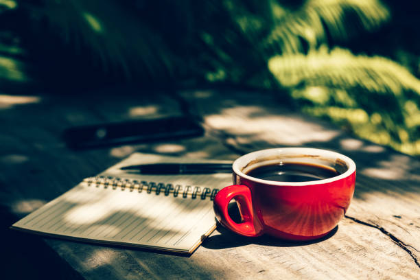 Cup of coffee and opened notebook standing on wooden balcony with lake background