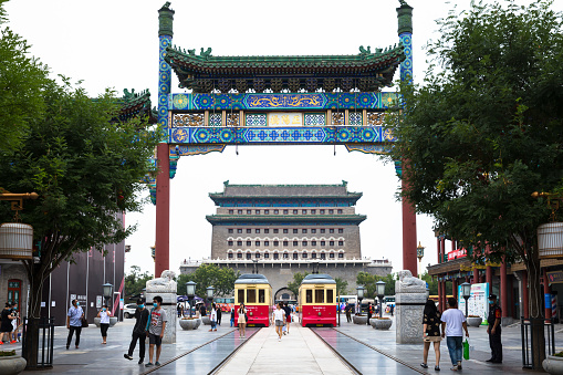 BEIJING, CHINA – August 06, 2020: Tourists wearing masks hanging out at Qianmen memorial archway, with zhengyang gate and tramcar in the background