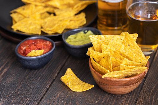 Nachos with guacamole, red chilli sauce and beer  on wooden table The most famous Mexican snack background.
