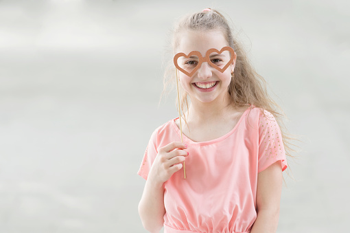 The goggles are accessory for her face. Little child looking happy through goggles props. Funny small girl with heart shaped goggles on stick. Cute kid smiling with fancy party googles, copy space.