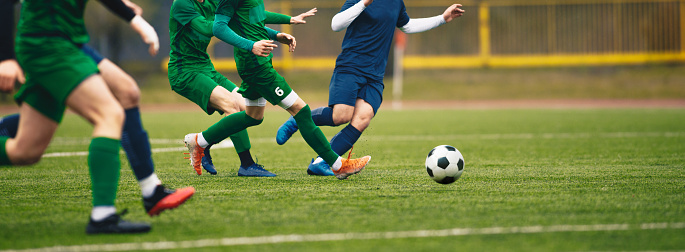 Teenagers in soccer duel. Boys in two football teams running after classic soccer ball. Horizontal sports background. Legs of young players on football pitch