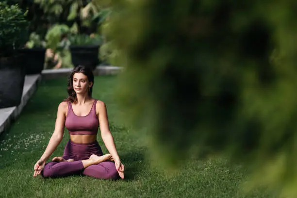 Woman practicing yoga performing yoga-asanas outdoors. Young attractive slim fitness girl in bodysuit relaxing and doing exercises.