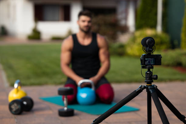 istock Male athlete sitting on exercise mat and making vlog at backyard. 1272395743