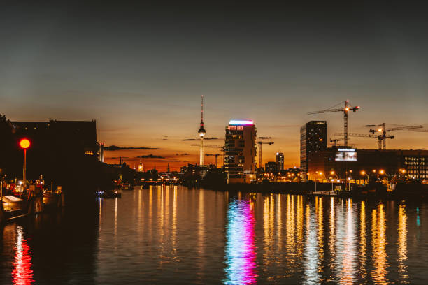 As night falls, the river reflects the soft lights of the city skyline. Boats rest quietly in the water, while a peaceful atmosphere envelops the scene.