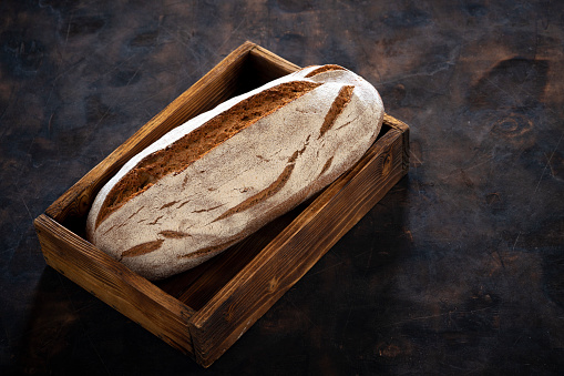 Wholegrain rye bread loaf in wooden box tray over dark wooden background vintage