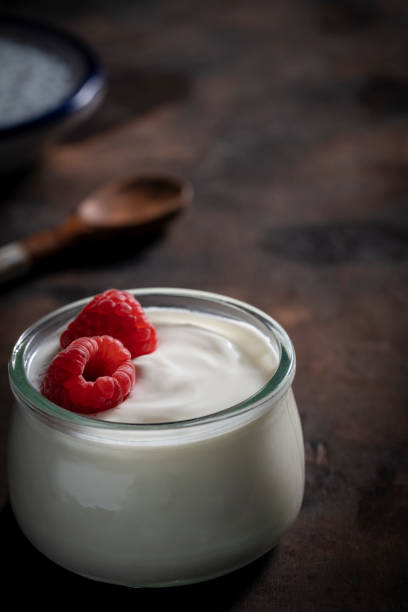 yogurt jar with rapsberries in moody low key dark wood - milk old fashioned retro revival still life imagens e fotografias de stock