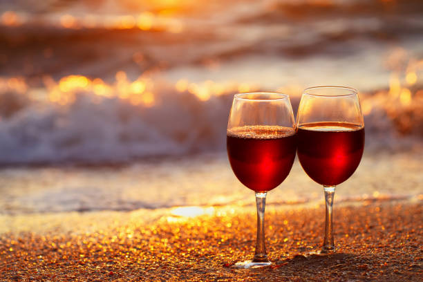 two glasses of red wine on the sea beach at sunset