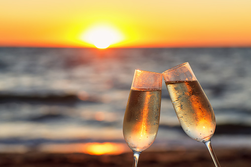two glasses of champagne making toast and sea at sunset on the background