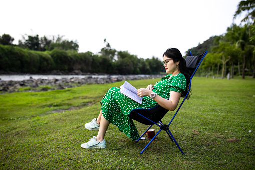 asian pregnant woman reading a book when taking vacations