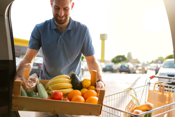 istock Young man packing box with fruit and vegetables into a car trunk 1272408178