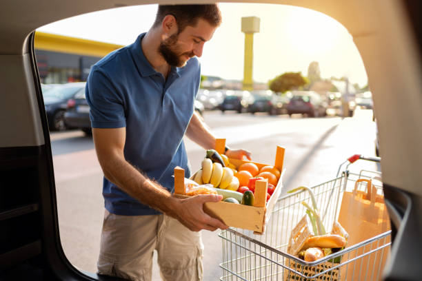 istock Young man moving crate with fruit and vegetables into a car trunk 1272408185