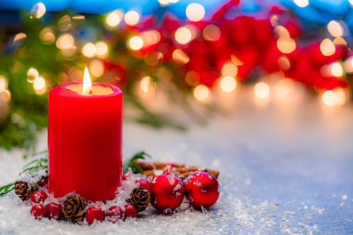 Christmas backgrounds: red burning Christmas with Christmas decoration. The composition is at the left of an horizontal frame leaving useful copy space for text and/or logo at the right.\nString light and Christmas decoration are out of focus at background. Predominant colors are red and blue. High resolution 42Mp studio digital capture taken with Sony A7rII and Sony FE 90mm f2.8 macro G OSS lens