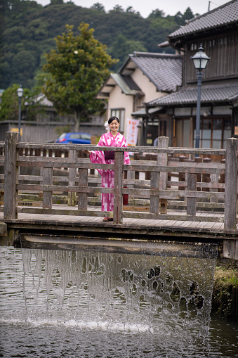 Young woman in yukata standing on old wooden bridge, water in falling