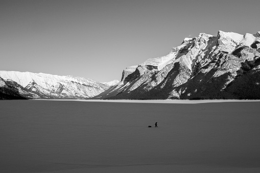 Lone person walks across a frozen lake surrounded by mountains in the Canadian Rockies