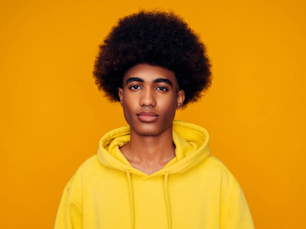 uomo afroamericano con i capelli afro che indossa la felpa con cappuccio e si trova su uno sfondo giallo isolato - afro americano foto e immagini stock