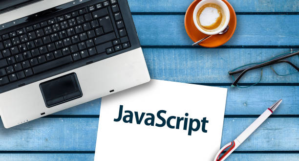 Paper width word JavaScript and laptop, glasses and coffee on wooden table