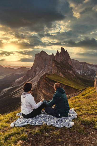 istock Couple sitting in a meadow and watching the sunset 1272413996