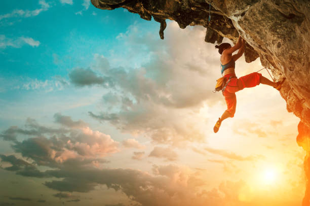 femme athlétique grimpant sur le roche de falaise en surplomb avec le fond de ciel de coucher du soleil - climbing mountain climbing rock climbing women photos et images de collection