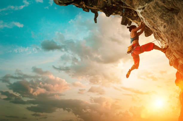 日没の空の背景と張り出し崖岩に登るアスレチック女性 - overhanging ストックフォトと画像
