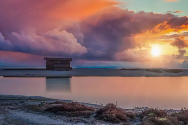 wooden shed by the sea at dawn with dramatic cloudy sky and sun flare