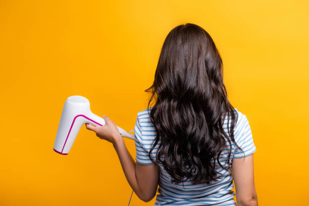 vue arrière de la femme brune avec des boucles retenant sèche-cheveux isolés sur le jaune - cheveux noirs photos et images de collection