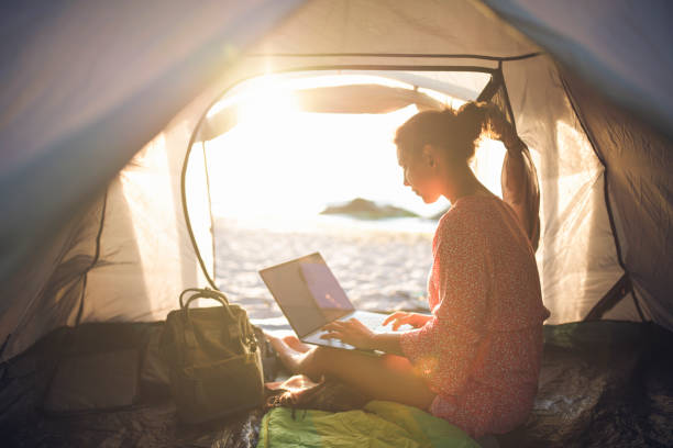 istock Woman Using Technology At Sunrise In Camping Tent On The Beach. 1272421996