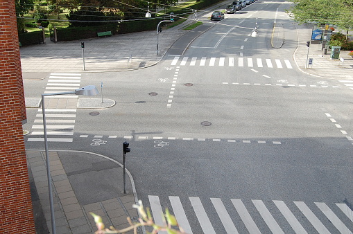 An empty crossroad in the sunlight with parked cares to the left.