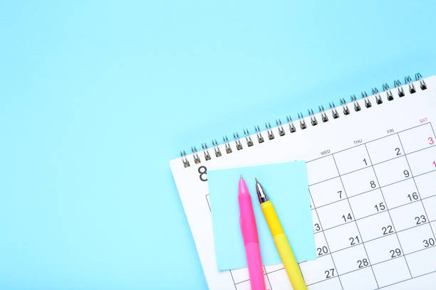 istock Calendar page with sticky note and pens on blue background 1272427298