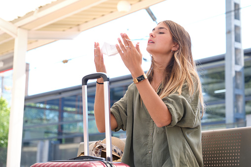 Young woman removing her face mask at a train station. Travel and coronavirus concept.