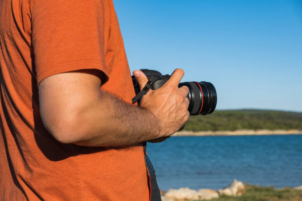 istock Anonymous man holding DSLR camera in hands next to seashore 1272436785