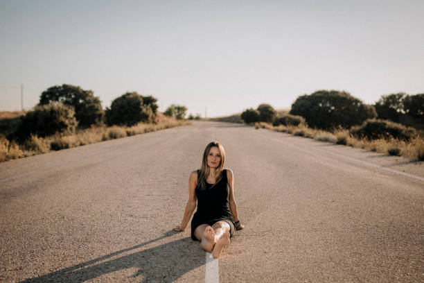 Una mujer con vestido negro sentada en una carretera vacía - foto de stock