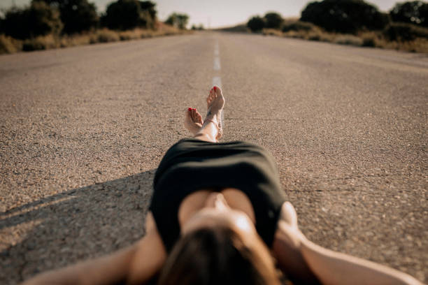 Una mujer con vestido negro tumbada en una carretera vacía - foto de stock