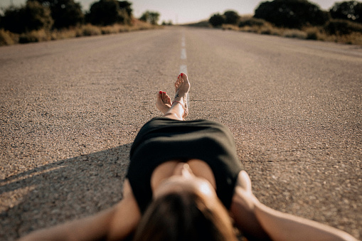 A photo of a woman lying down, in a black dress, on an empty road.