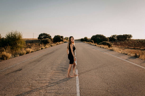 A woman in a black dress on an empty road - fotografia de stock