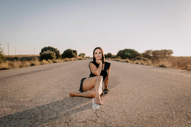 Una mujer con vestido negro sentada en una carretera vacía - foto de stock