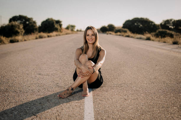 Una mujer con vestido negro sentada en una carretera vacía - foto de stock