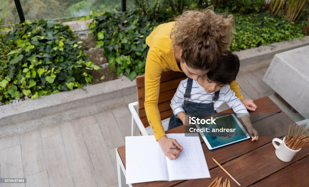 Mother assisting her son with his e-learning while using a digital tablet Mother assisting her son with his e-learning while using a digital tablet â back to school concepts. **DESIGN ON SCREEN WAS MADE FORM SCRATCH BY US** Deck Stock Photo