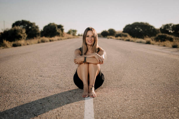 Una mujer con vestido negro sentada en una carretera vacía - foto de stock
