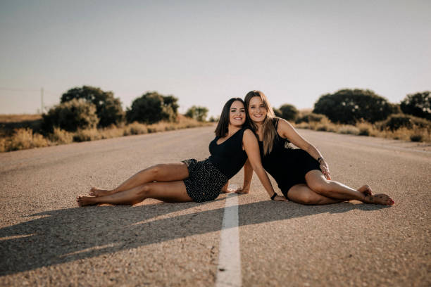 Two beautiful women sitting on a road - fotografia de stock