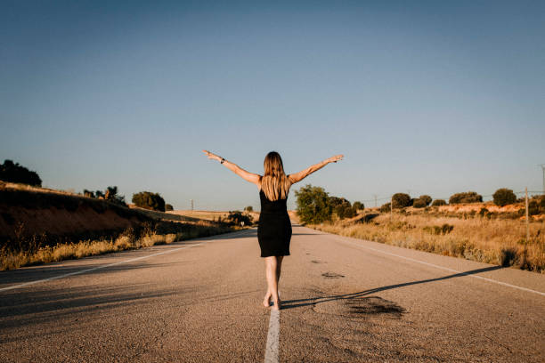 Una mujer con vestido negro en una carretera vacía - foto de stock