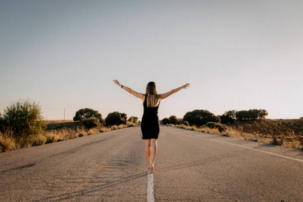 Una mujer con vestido negro en una carretera vacía - foto de stock