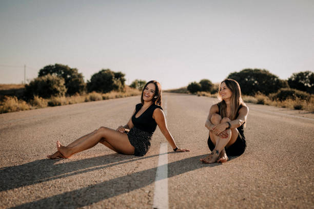 Dos mujeres bellas sentadas en una carretera - foto de stock