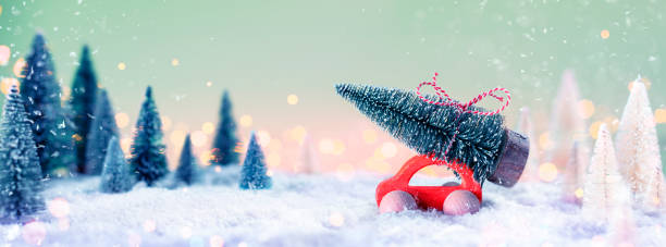 istock Red Car Carrying A Christmas Tree In Defocused Snowy Landscape 1272441792