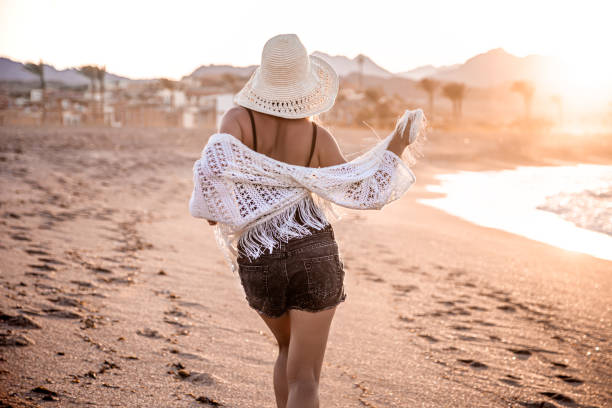 istock A woman in a hat walks at sunset on the beach rear view 1272443365