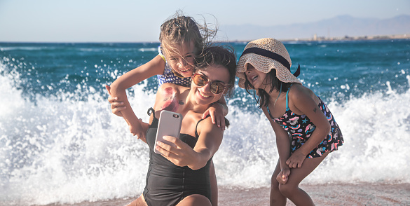 A mother with a child takes a selfie against the background of the sea and sea waves. The concept of family and recreation